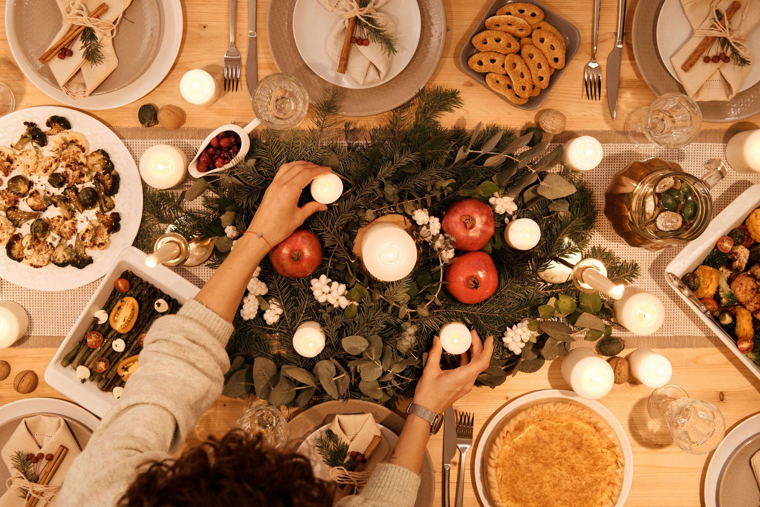A holiday table filled with candles, greenery, and shared dishes as hands adjust the centerpiece. Do sensory experiences make the holidays feel overwhelming? Working with a registered dietitian in Raleigh, NC, can help create calming food routines that support emotional regulation.
