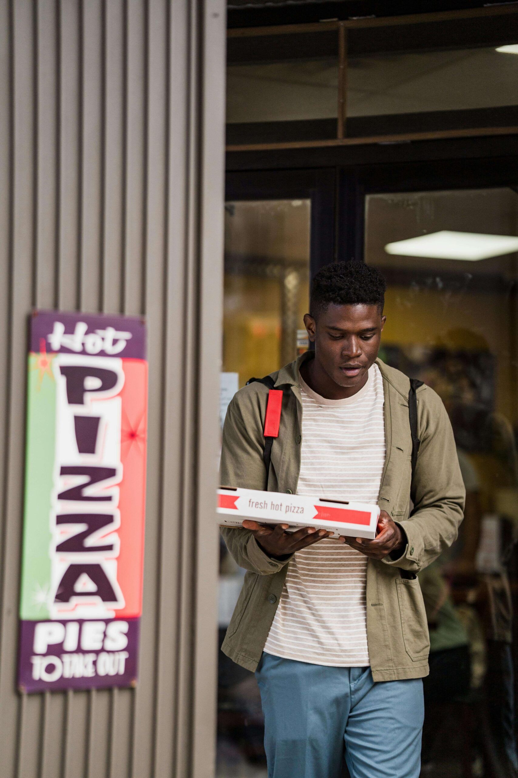 Young man holding a pizza box outside a restaurant, illustrating the reality of relying on takeout when executive dysfunction makes cooking overwhelming. Nutrition counseling in Raleigh, NC, with a registered dietitian in Raleigh, NC, helps neurodivergent adults build sustainable food systems.