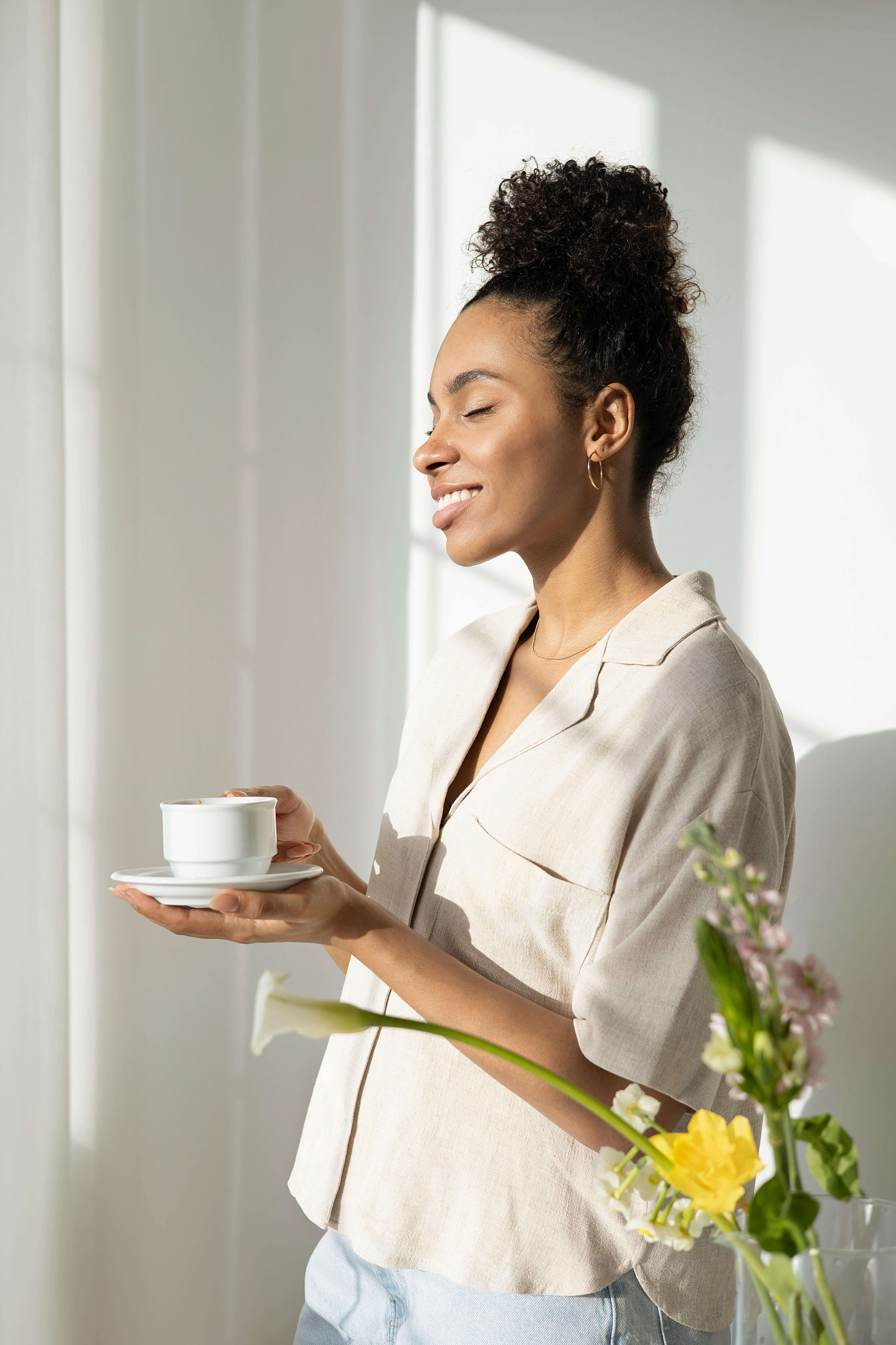 A woman standing peacefully in natural light, holding a cup and smiling with her eyes closed. Nutrition counseling in Raleigh, NC with a registered dietitian in Raleigh, NC supports your whole well-being—helping you feel more grounded, attuned, and cared for beyond just food choices.