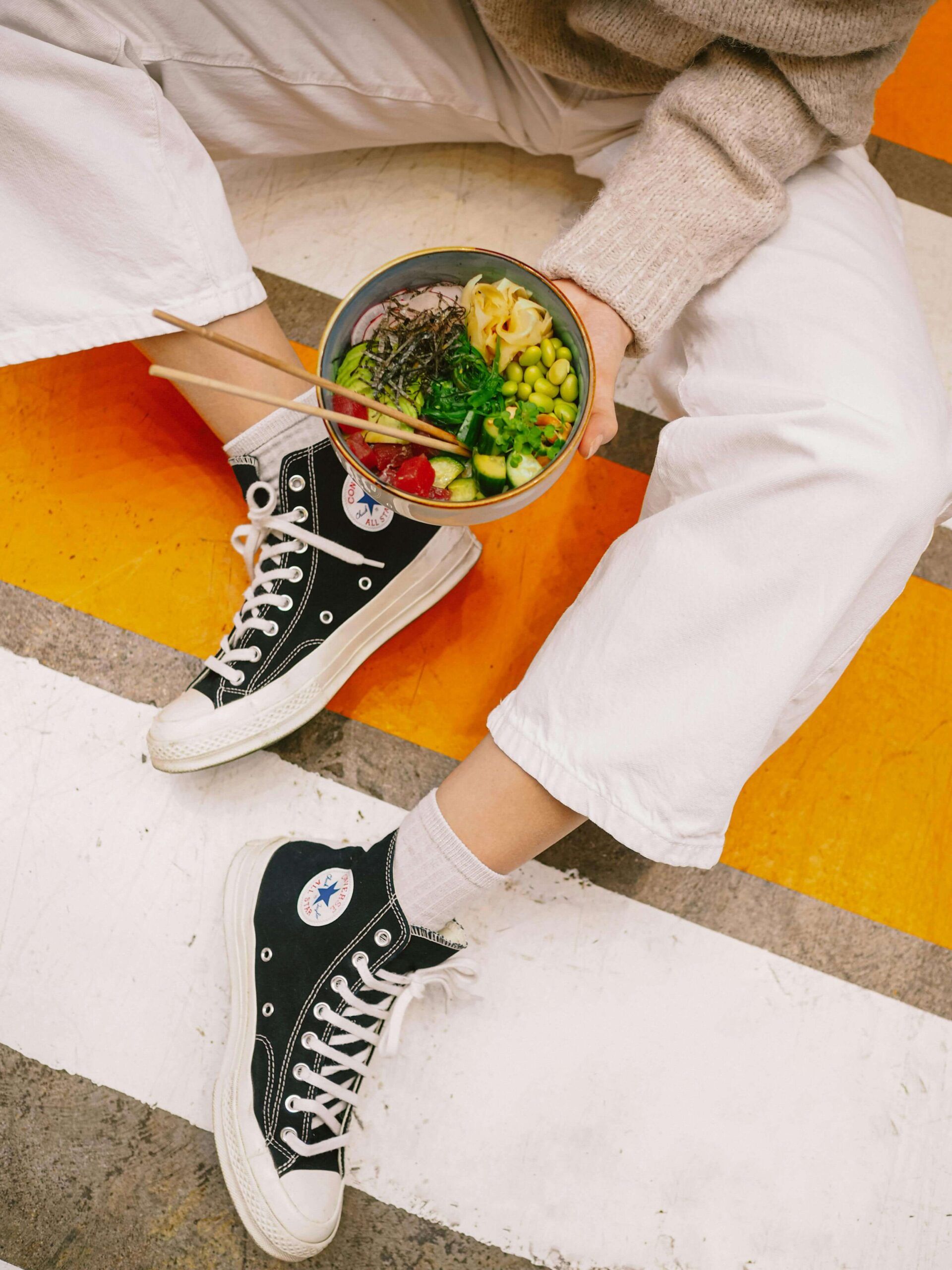 Person sitting casually in white pants and black Converse sneakers, holding a colorful bowl of fresh food—capturing a relaxed, nourishing moment that reflects the support of a nutritional therapist in Raleigh, NC and the personalized approach of nutritional counseling in Raleigh, NC.