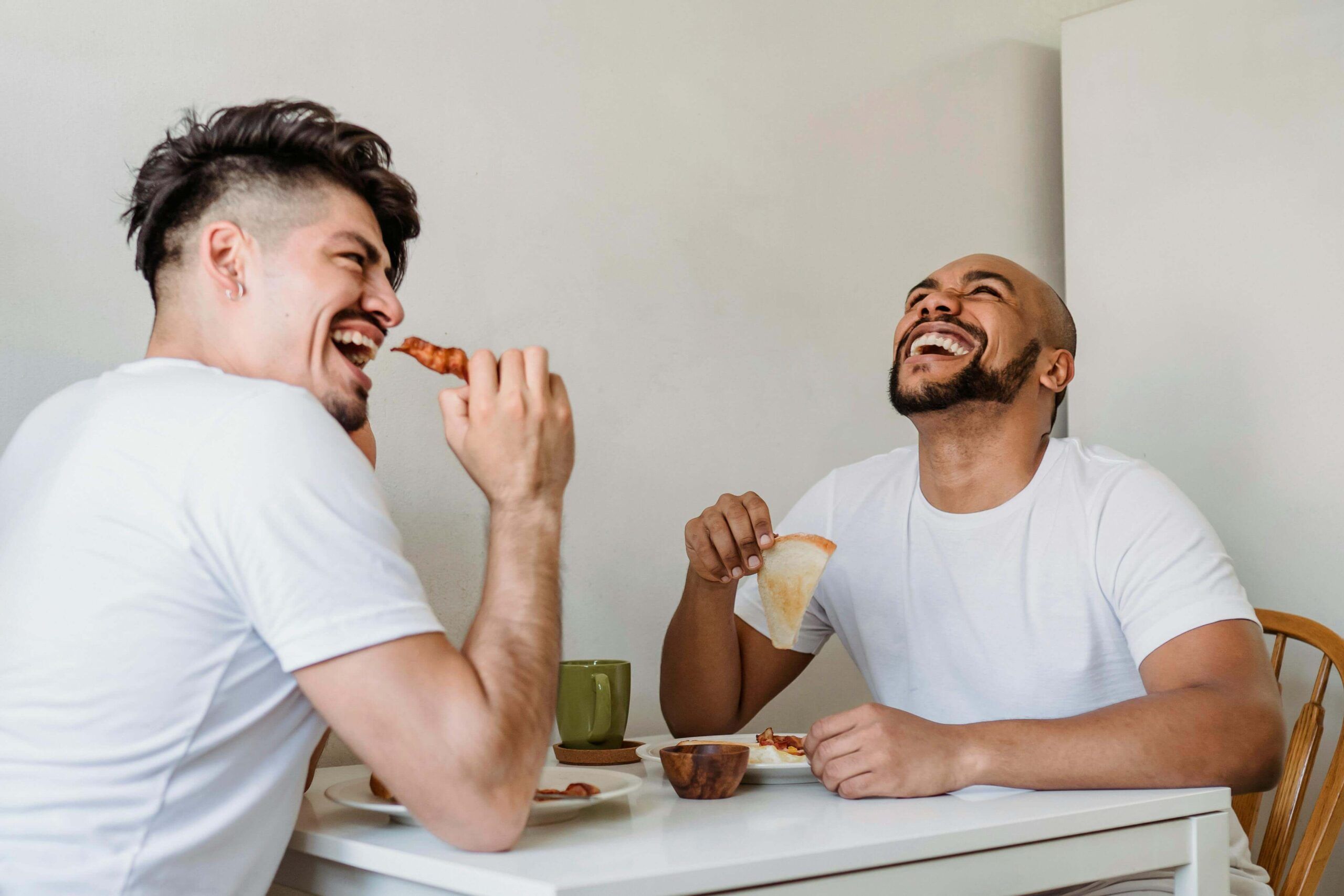 Two men laugh and enjoy a relaxed breakfast together, illustrating the joy and connection that can come from working with a registered dietitian in Raleigh, NC through personalized nutritional counseling in Raleigh, NC.
