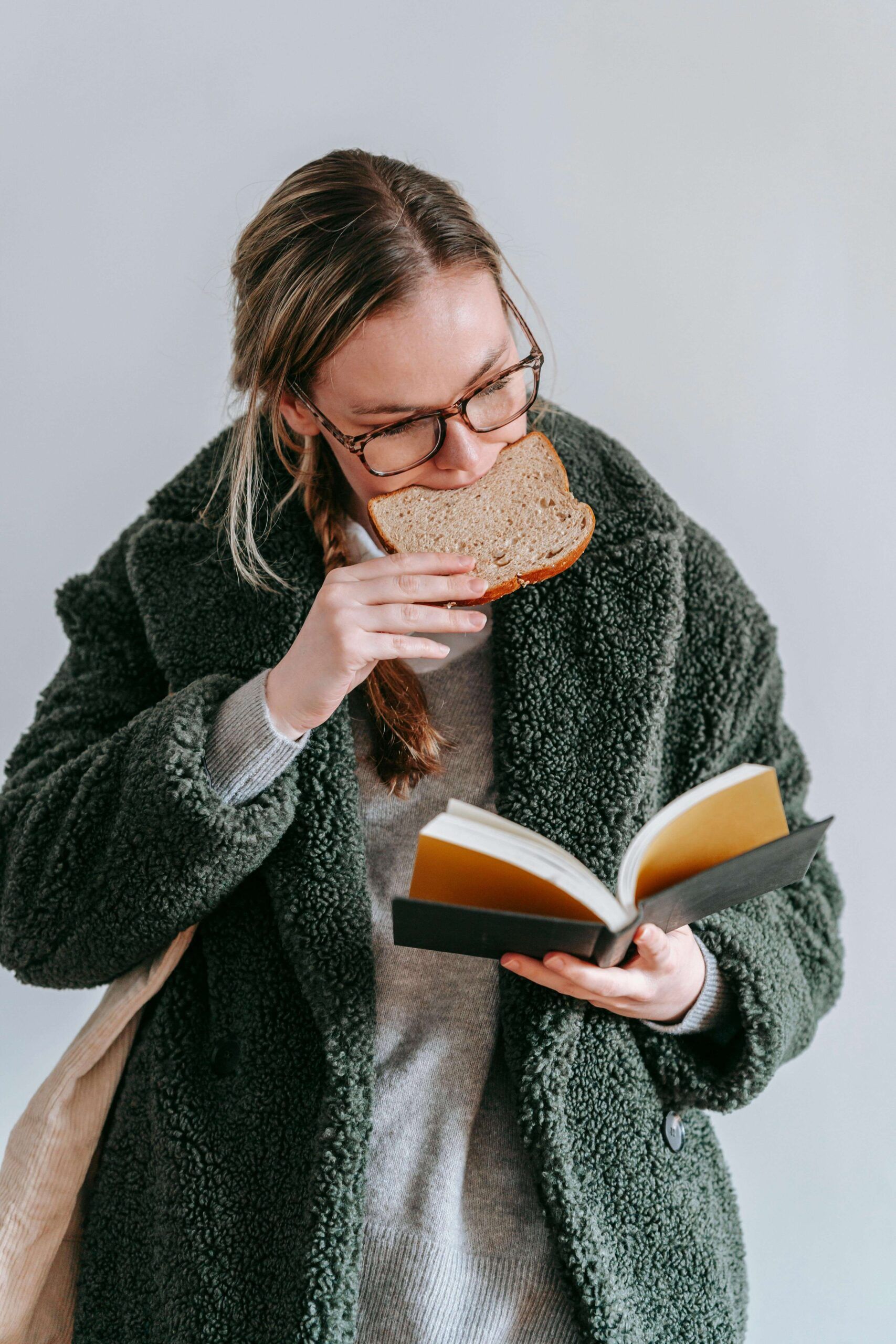 A woman in glasses reads a book while eating a slice of bread, reflecting the exhaustion of researching nutrition alone — nutrition counseling in Raleigh, NC and support from a registered dietitian in Raleigh, NC can help when information isn't enough.