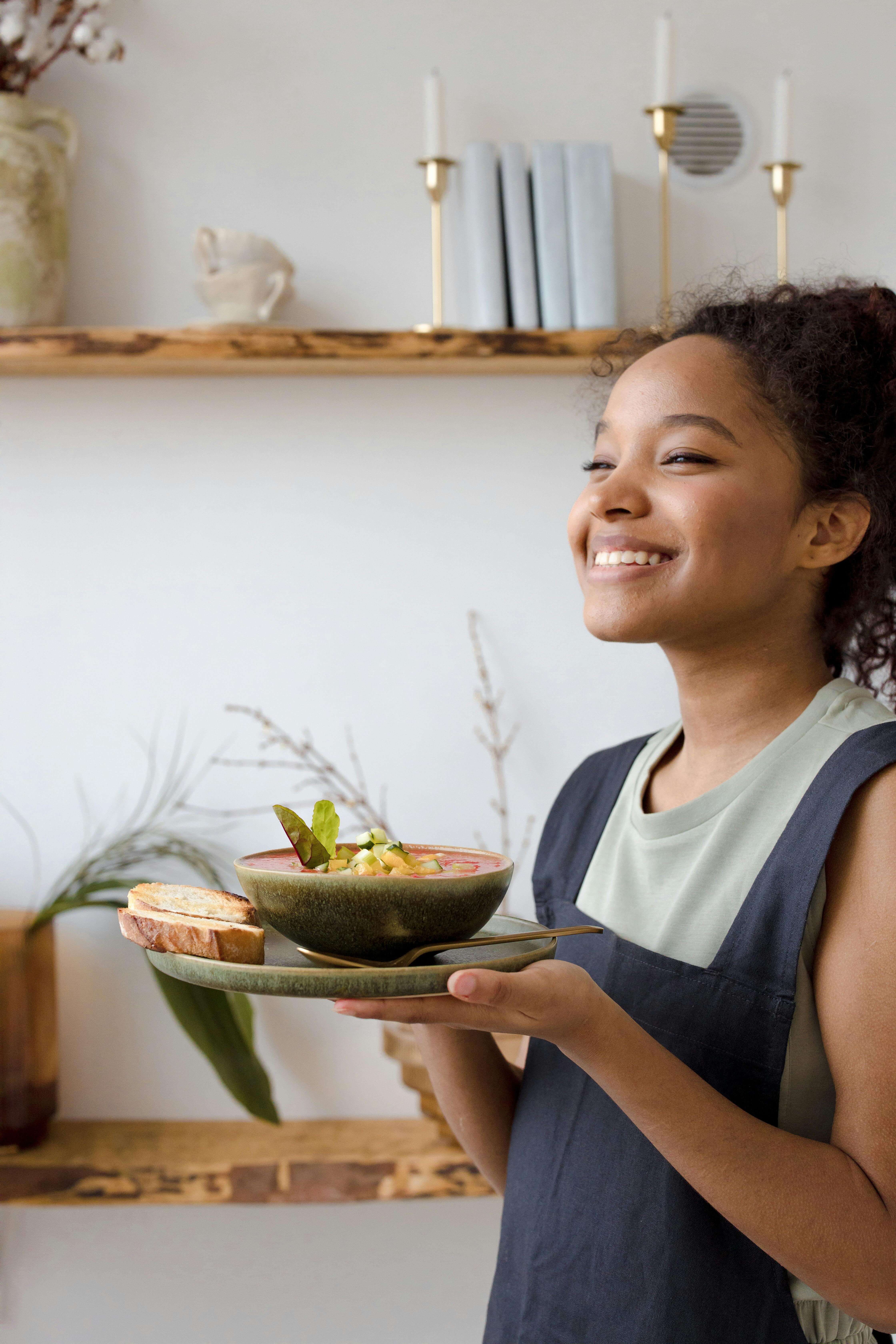 A smiling young woman holds a nourishing bowl of soup and bread, symbolizing the confidence and ease that can come from working with a registered dietitian in Raleigh, NC and receiving personalized nutrition counseling in Raleigh, NC.