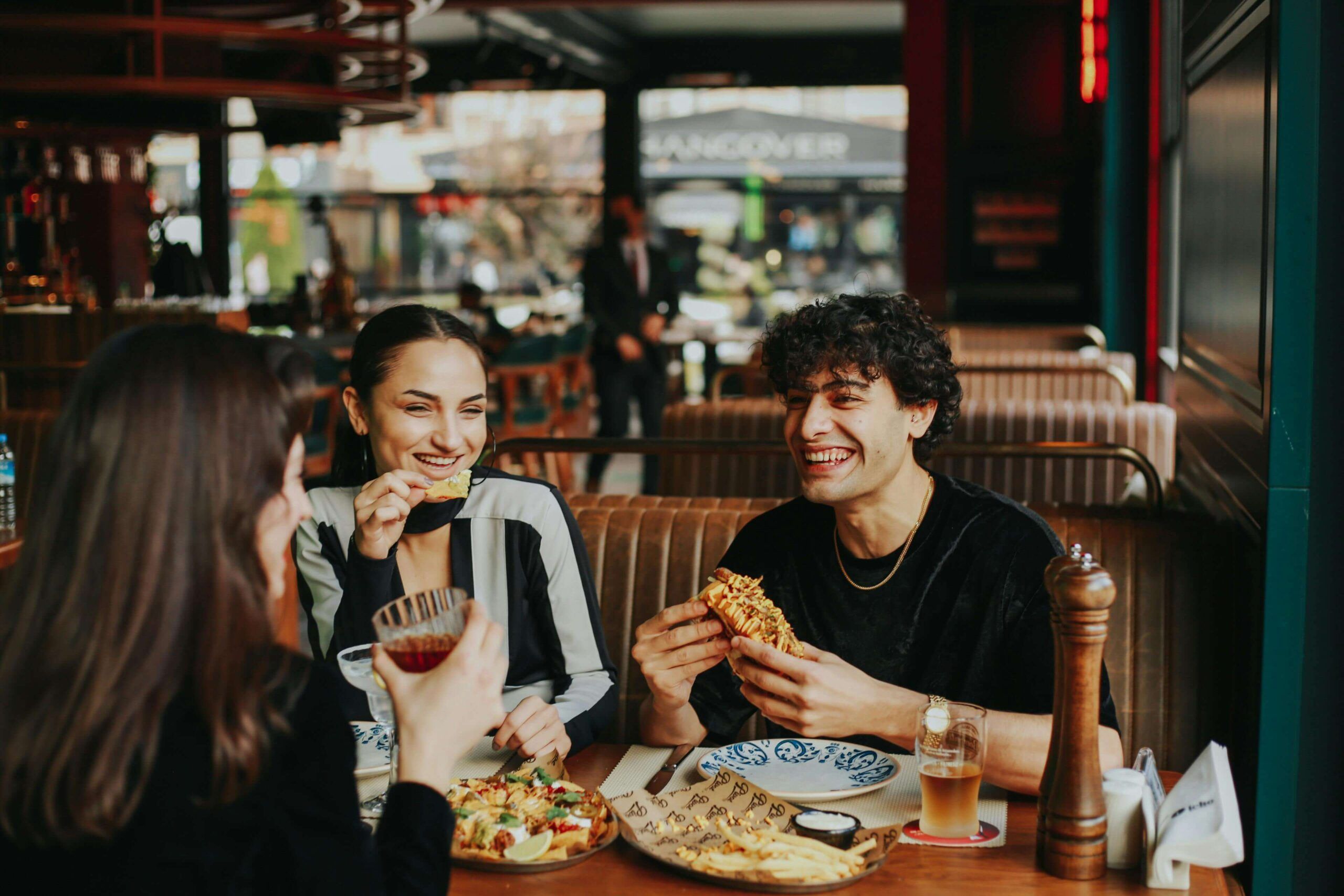Three friends laughing and enjoying a meal together at a restaurant, illustrating the connection between food and social well-being. Support from a registered dietitian in Raleigh, NC through nutrition counseling in Raleigh, NC can help reduce meal anxiety and bring ease back to eating in social settings.