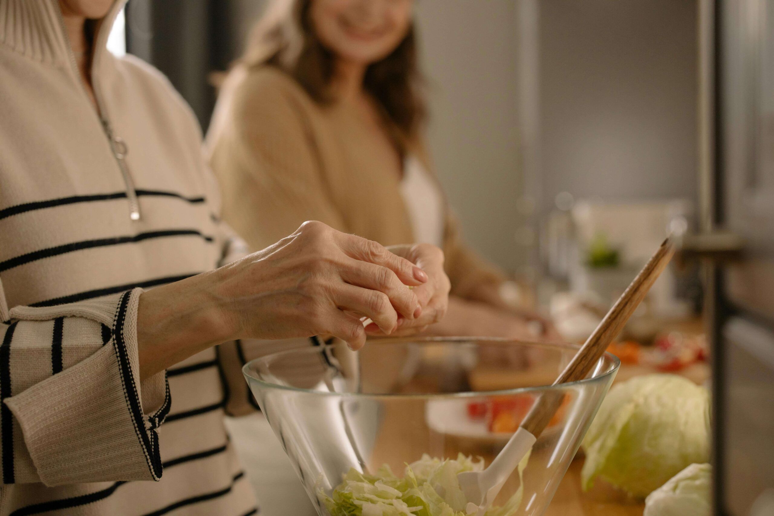 Two women preparing a fresh salad together in a warmly lit kitchen, symbolizing intuitive eating and connection. This image reflects the supportive guidance of a registered dietitian in Raleigh, NC, and the compassionate, individualized approach found in nutritional counseling in Raleigh, NC for navigating menopause.