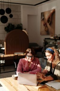 Two women smile while meeting over a laptop and food, reflecting the collaborative, supportive approach of a registered dietitian in Raleigh, NC and nutritional counseling in Hendersonville, NC.