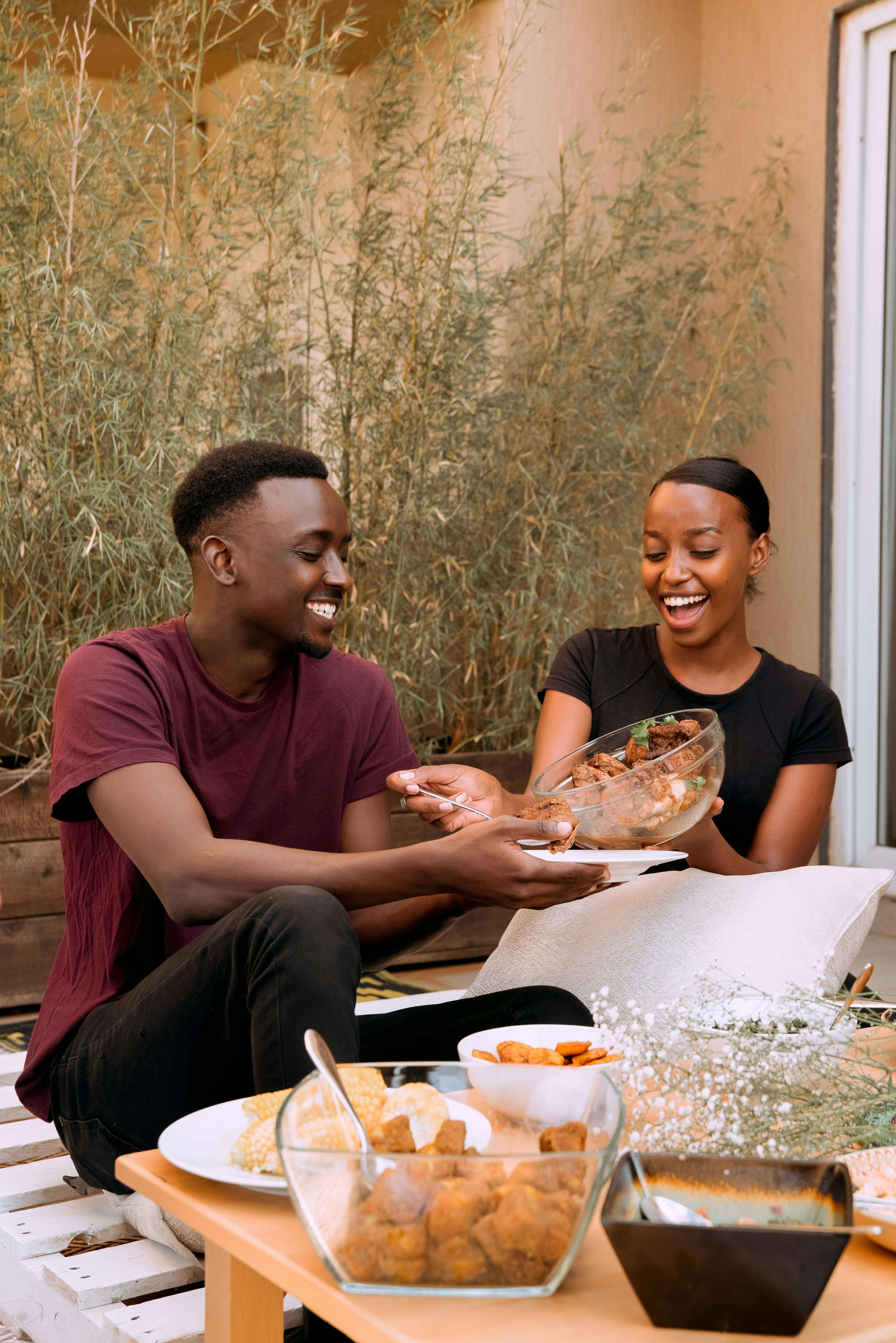 Two friends smile while sharing a meal together outdoors, representing the supportive, connection-based approach of working with a registered dietitian in Raleigh, NC and a nutritional therapist in Raleigh, NC.