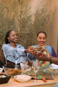 Two women smiling and sharing a bowl of food at a joyful summer gathering, representing the compassionate, inclusive support offered by a registered dietitian and nutritional therapist in Raleigh, NC.