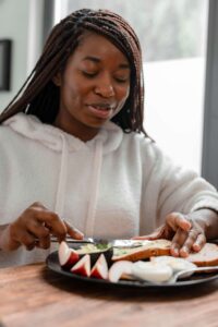 Black woman in a cozy hoodie spreads avocado on toast at a kitchen table, reflecting a moment of calm supported by binge eating disorder therapy in Asheville, NC and guidance from a registered dietitian in Raleigh, NC.