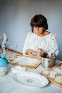 Older woman hand-folding dumplings at a kitchen table, surrounded by ingredients, representing how intuitive eating can be a meaningful, culturally grounded part of life transitions like menopause—with support from a nutritional therapist in Raleigh, NC offering nutrition counseling in Raleigh, NC.