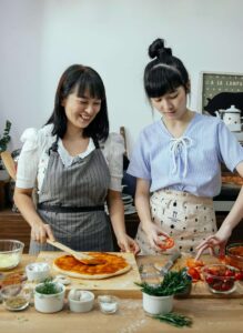 Two women prepare a homemade pizza together in a cozy kitchen, enjoying the cooking process with fresh ingredients like tomatoes and herbs. This image reflects the supportive, non-diet approach encouraged in nutritious counseling for eating disorders in Asheville, NC, and aligns with the values of a registered dietitian in Raleigh, NC who supports intuitive eating during menopause.