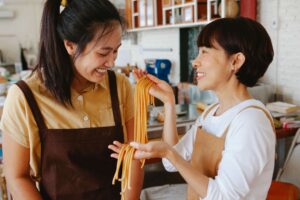  Two women smile while preparing fresh pasta together in a kitchen. Nutrition therapy in Raleigh, NC, and medical nutrition therapy in Raleigh, NC, can empower you to take charge of your health with confidence.