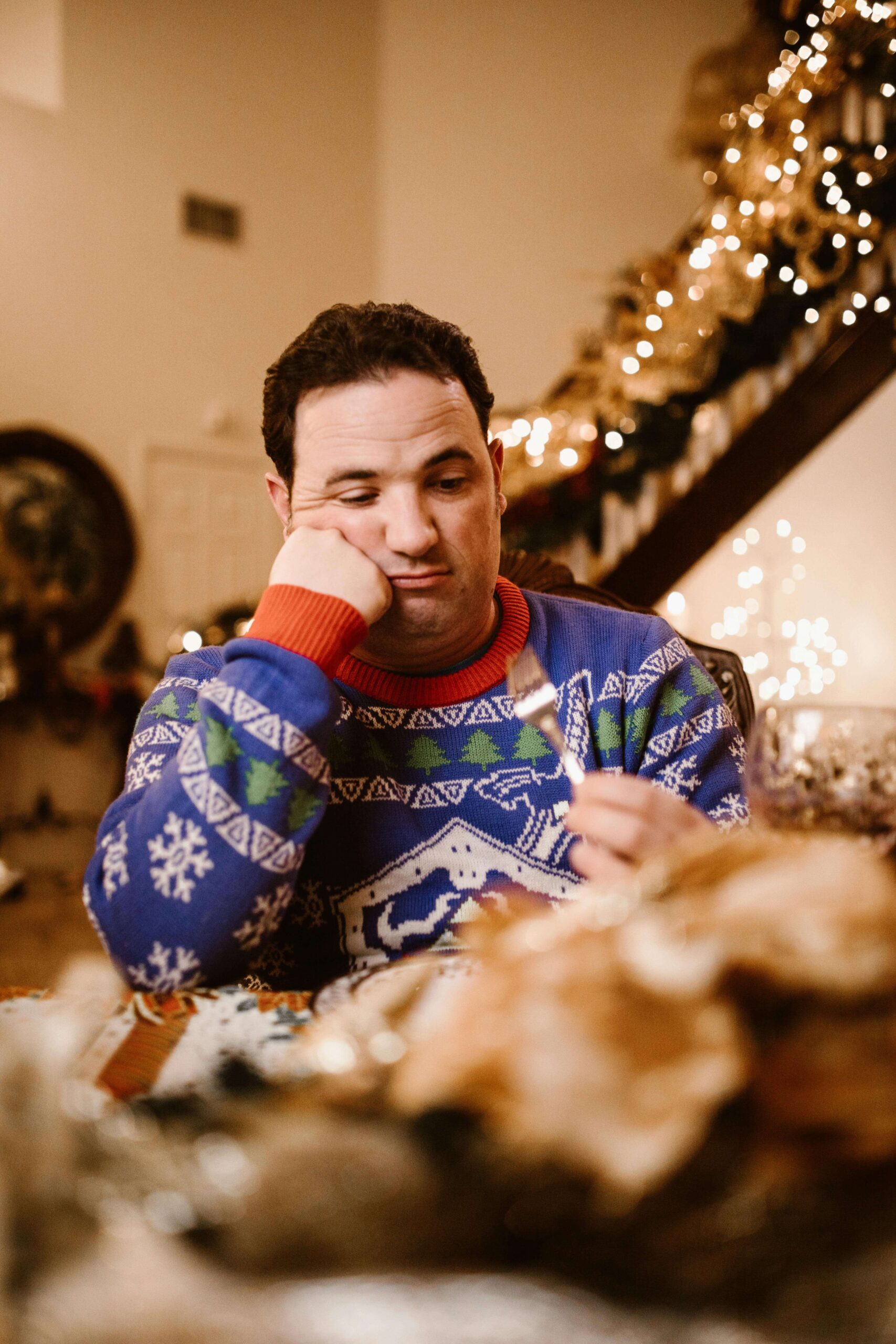 A man sits at a holiday table looking uncomfortable. When the holidays overstimulate the senses, meals can feel emotionally exhausting. Nutrition counseling in Raleigh, NC, can help manage sensory triggers and support emotional regulation around food.