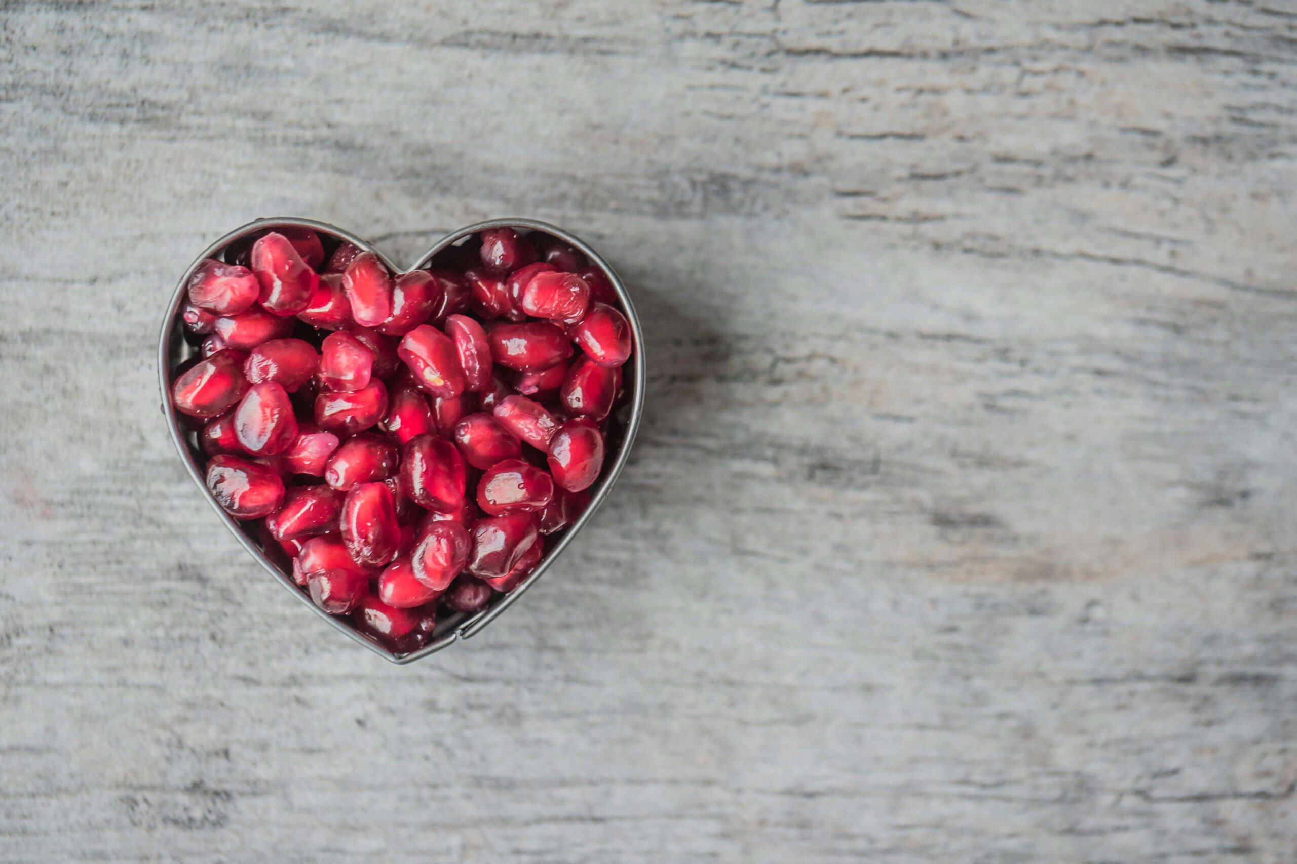 Heart-shaped bowl filled with pomegranate seeds, symbolizing heart health supported through compassionate nutrition counseling in Raleigh, NC with a registered dietitian in Raleigh, NC using HAES principles.