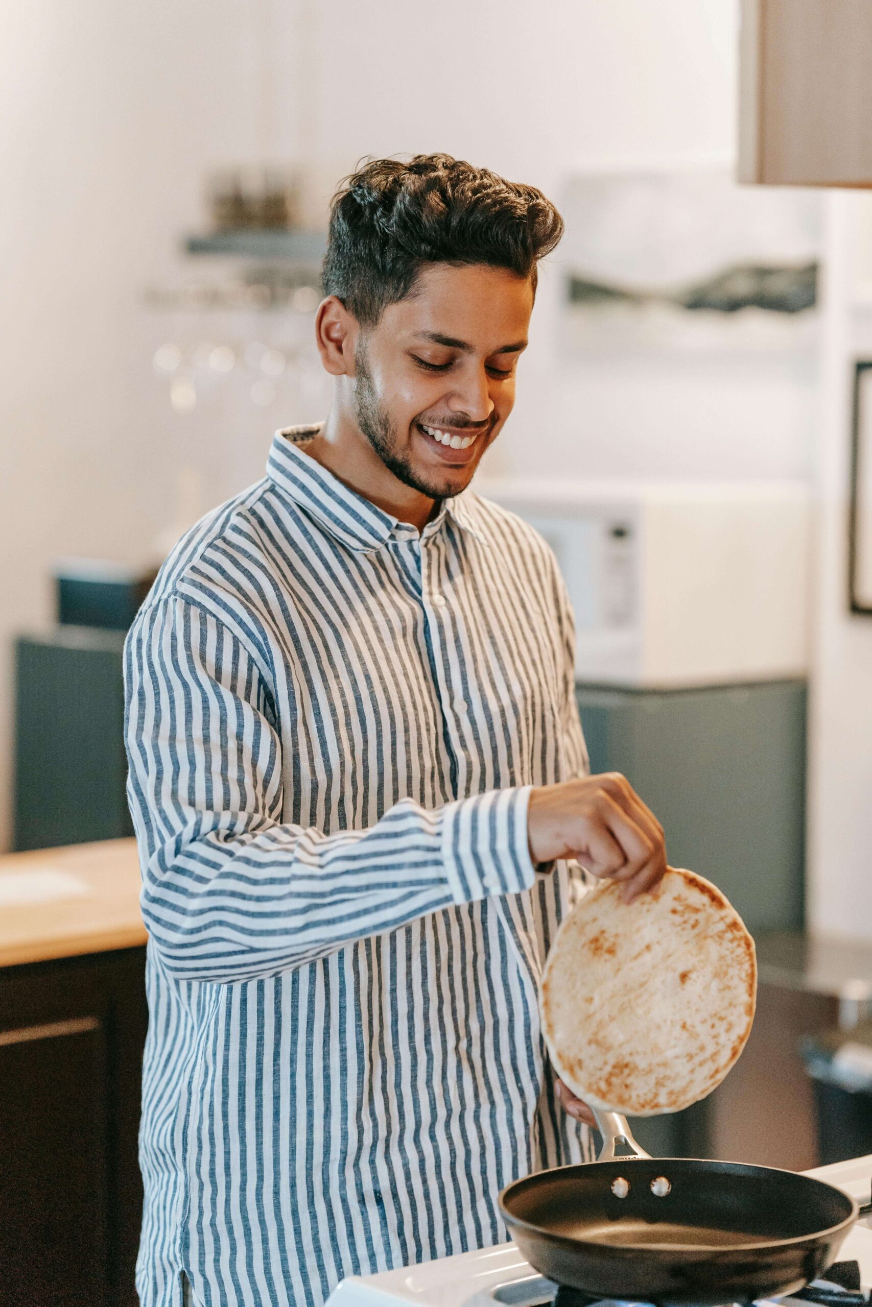 Man smiling while making a flatbread or tortilla in his kitchen, representing the joyful, shame-free relationship with nourishment supported through nutrition therapy in Raleigh, NC with a registered HAES dietitian in Raleigh who honors all eating experiences.