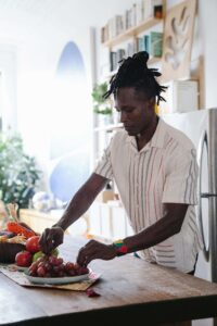 A man with dreadlocks arranges fresh fruit at a kitchen counter, representing the everyday relationship with nourishment that nutrition therapy in Raleigh, NC supports — a nutritional therapist in Raleigh, NC can help when eating feels harder than it looks.