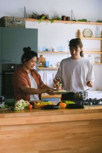 Two people cook together at a stovetop surrounded by fresh vegetables, representing the everyday relationship with nourishment supported through nutrition counseling in Raleigh, NC and medical nutrition therapy in Raleigh, NC.