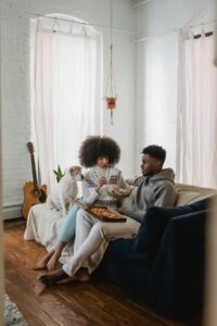 A woman and man relax on a couch with their dog, sharing a casual meal at home, reflecting the everyday moments of nourishing yourself that medical nutrition therapy in Raleigh, NC and nutrition counseling for well-being in Raleigh can help make feel easier.