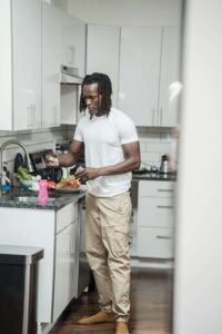 Doing Dishes | disordered eating therapy asheville, nc | nutrition counseling for eating disorders raleigh, nc | nutrition therapy raleigh, nc | nutritional therapist raleigh, nc | Raleigh, NC | Asheville, NC | Cary, NC A man with locs stands alone in a kitchen preparing a meal with fresh vegetables on the counter, representing the quiet, everyday moments around nourishment supported through medical nutrition therapy in Raleigh, NC and disordered eating therapy in Asheville, NC.